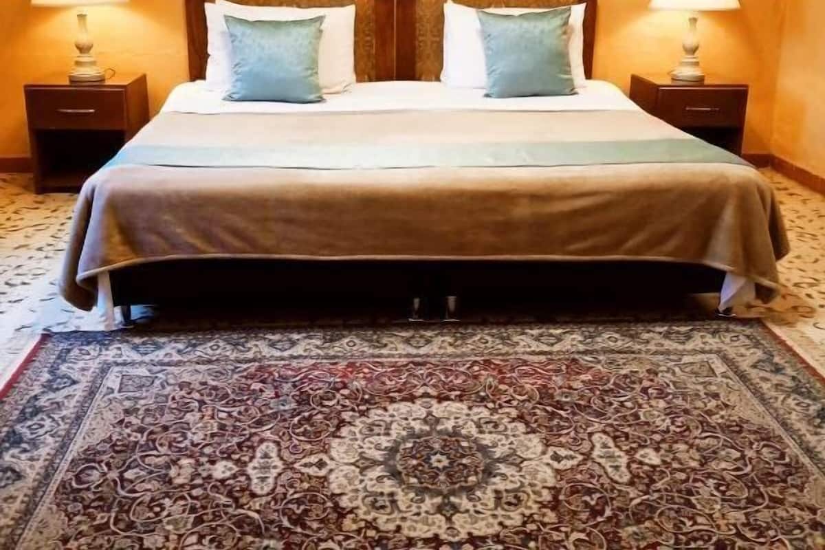 Une chambre d’hôtel avec un grand lit, deux lampes de chevet, un tapis à motifs et deux tableaux encadrés accrochés au mur.