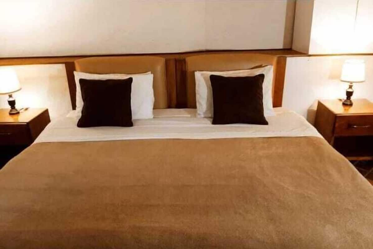 Une chambre d’hôtel avec un grand lit, deux tables de chevet et une petite table de nuit avec une lampe.