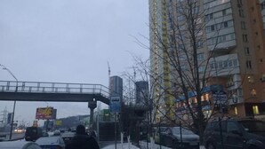 A city street with a pedestrian overpass, tall buildings, and parked cars. - Yourhostel Saperka (Kyiv)