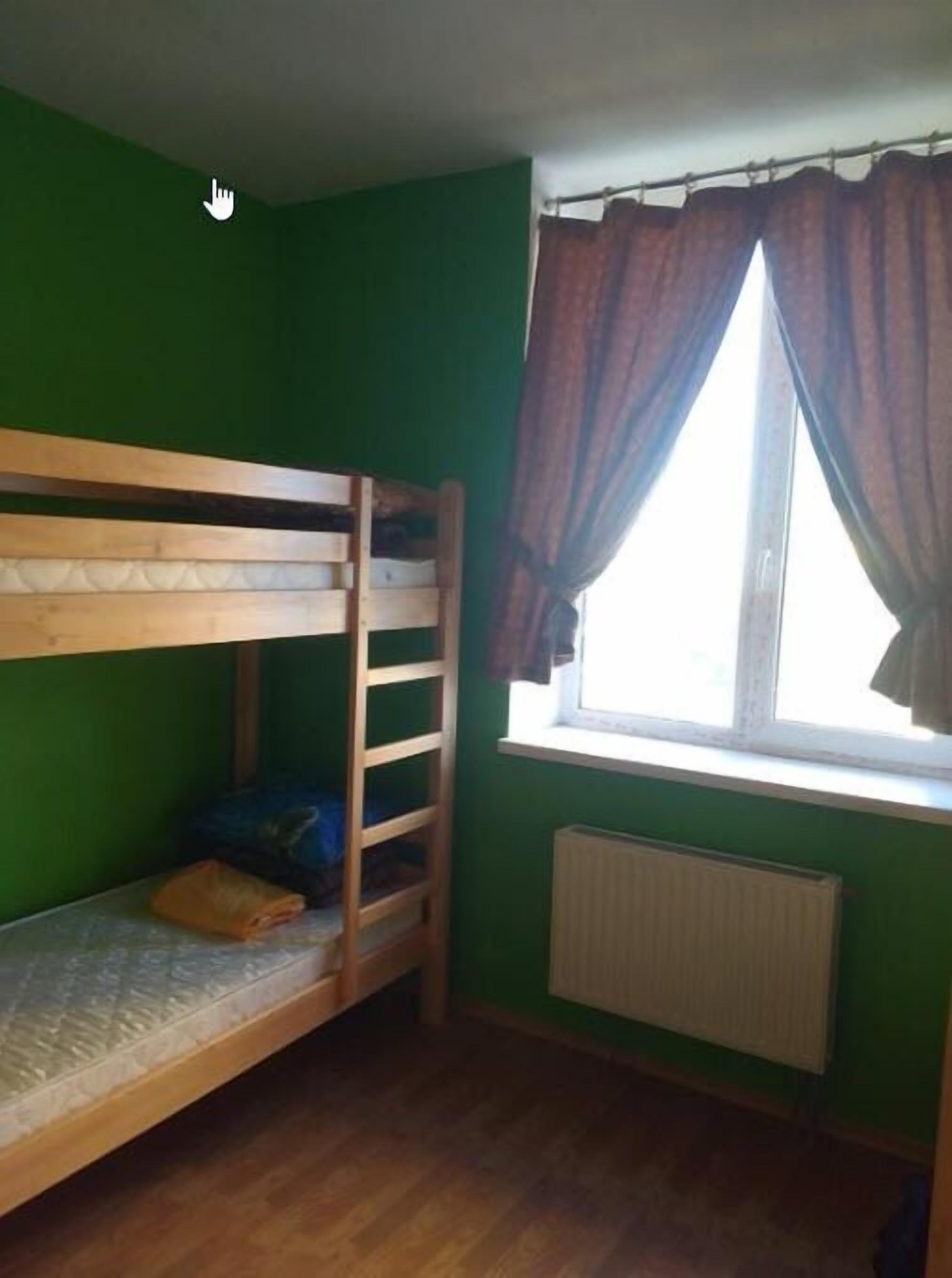A room with a bunk bed, a radiator, a window with curtains, and a green wall.
