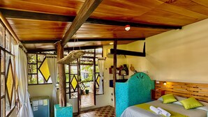 A room with a checkered floor, a bed with green pillows, a wooden ceiling, and a window with curtains. - Casa del Lago Lodging House (Puerto Ayora)