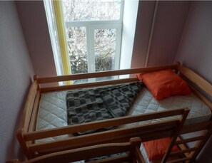 Un lit superposé avec un matelas et des oreillers, une fenêtre donnant sur des arbres et un rideau.