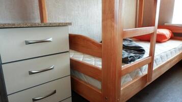Un lit superposé avec une structure en bois, un matelas et un oreiller orange. À gauche, on aperçoit une commode blanche avec des poignées argentées.