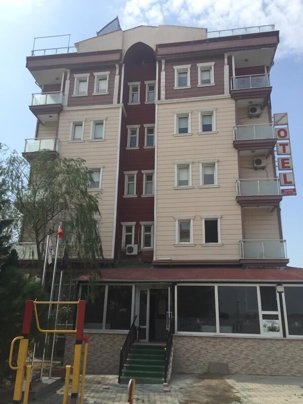 A multi-story hotel with balconies, a central entrance with a staircase, and a sign indicating it is a hotel.