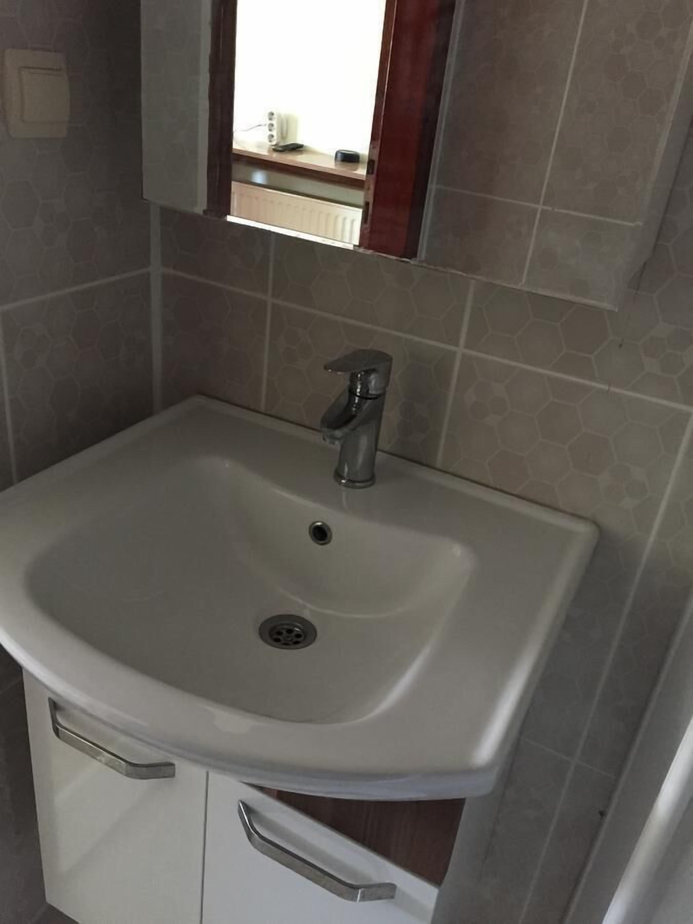 A bathroom with a white sink, a mirror above it, and a window with a view of the outside.