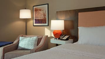 A hotel room with a bed, a chair, a nightstand with a lamp, and a painting on the wall.