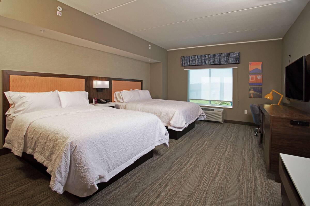 A hotel room with two beds, a desk, a television, and a window with a view.