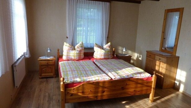 Un letto di legno con una coperta a quadri e cuscini, un comodino, uno specchio e una finestra con tende.