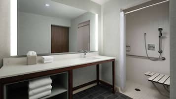 Un baño moderno con un espejo grande, dos lavamanos, una ducha con barra de apoyo y un perchero para toallas.