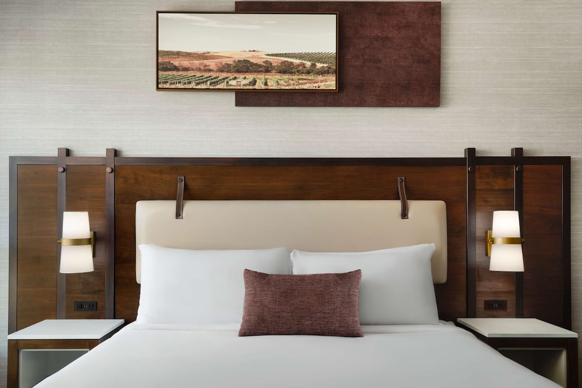 Ein Hotelzimmer mit einem großen Bett, zwei Nachttischen, einem Kopfteil und einem Wandbild.