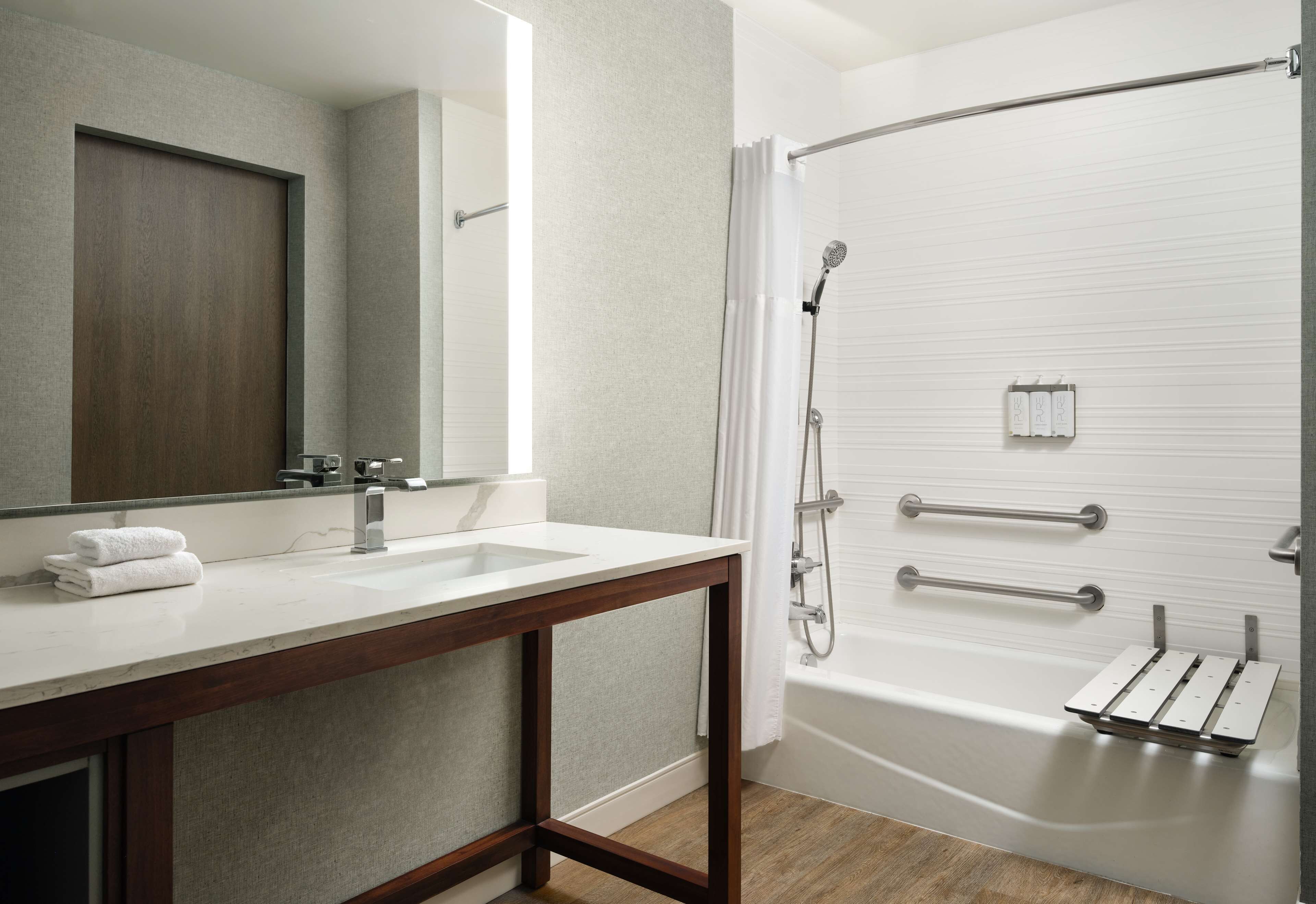 A modern bathroom with a wooden vanity, a large mirror, a bathtub, and a shower with grab bars.
