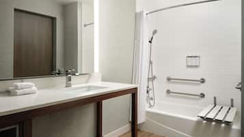A modern bathroom with a wooden vanity, a large mirror, a bathtub, and a shower with grab bars.