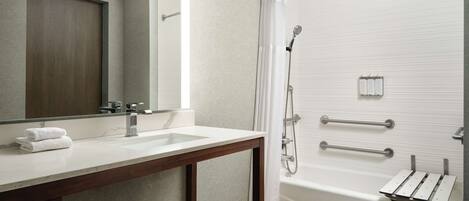 A modern bathroom with a wooden vanity, a large mirror, a bathtub, and a shower with grab bars.