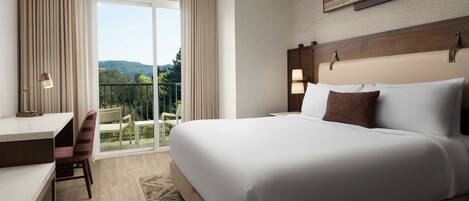 Habitación de hotel con una cama grande, un escritorio y una silla. Tiene un balcón con vistas al exterior.