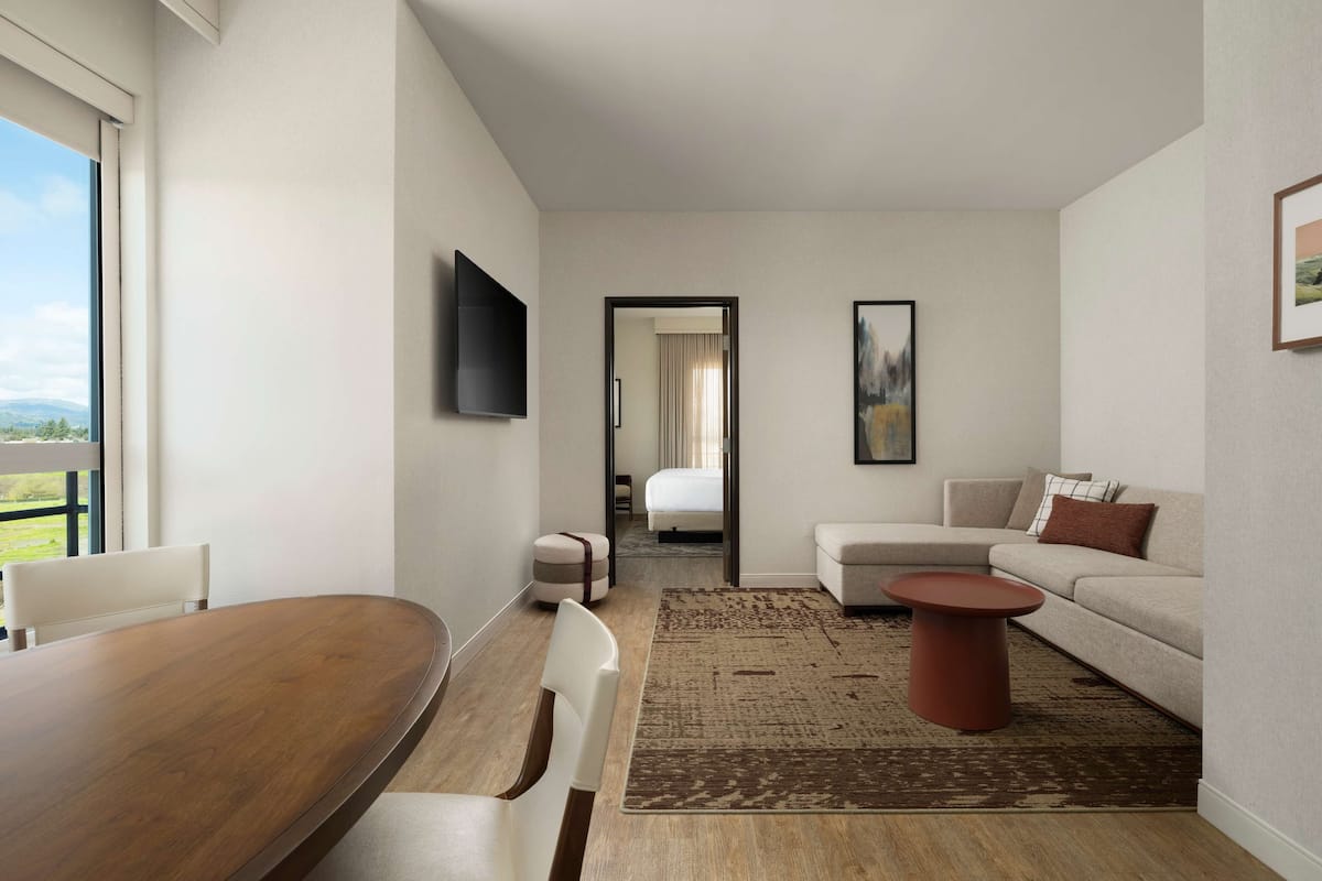 Ein modernes Hotelzimmer mit Essbereich, einer Couch, einem Fernseher und Blick ins Freie.