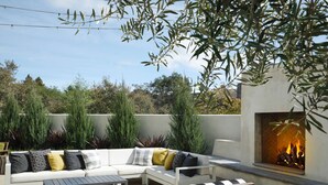 Eine Terrasse im Freien mit einem weißen Sofa, schwarzen und weißen Kissenstreifen und einer Feuerstelle.