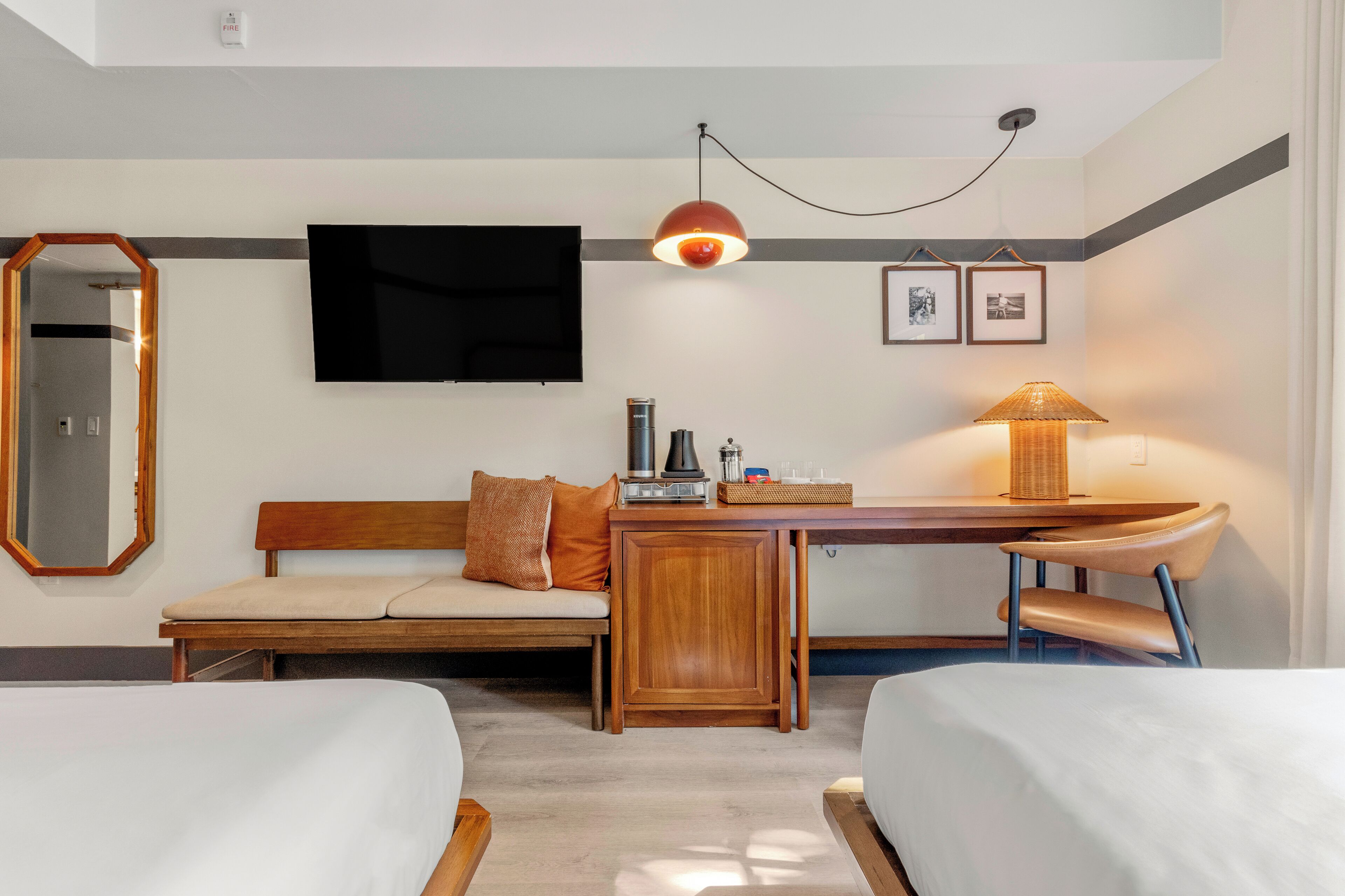 Quarto de hotel com duas camas, uma escrivaninha com abajur, televisão e quadros na parede.