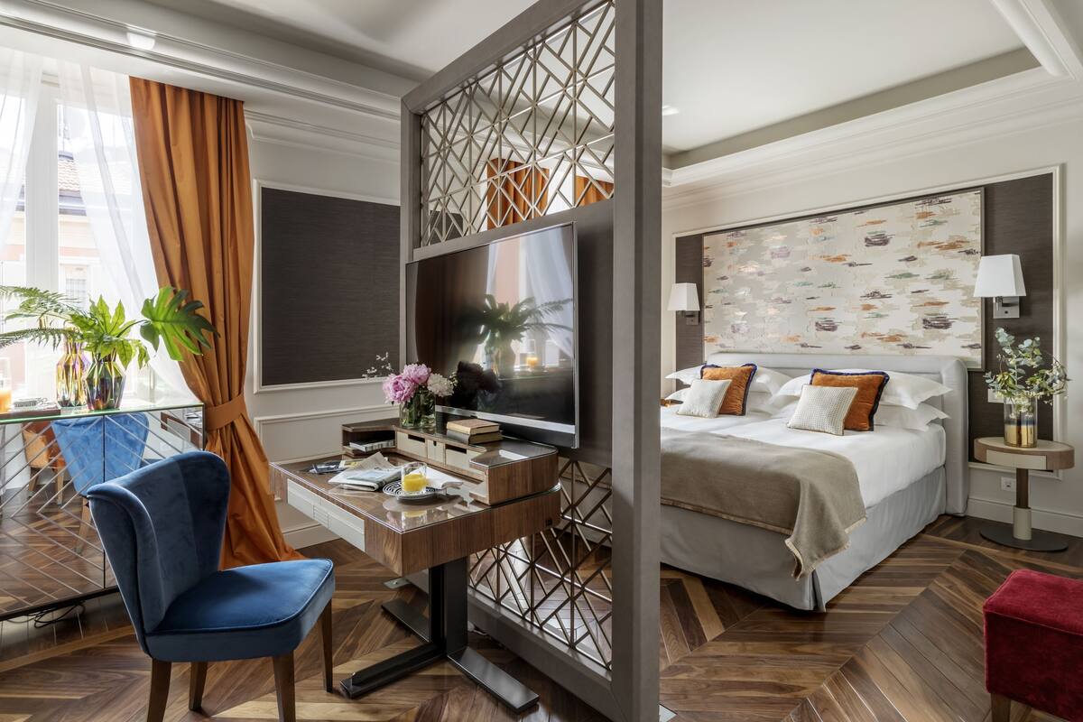A hotel room with a bed, a desk with a TV, a chair, and a view of the outside.
