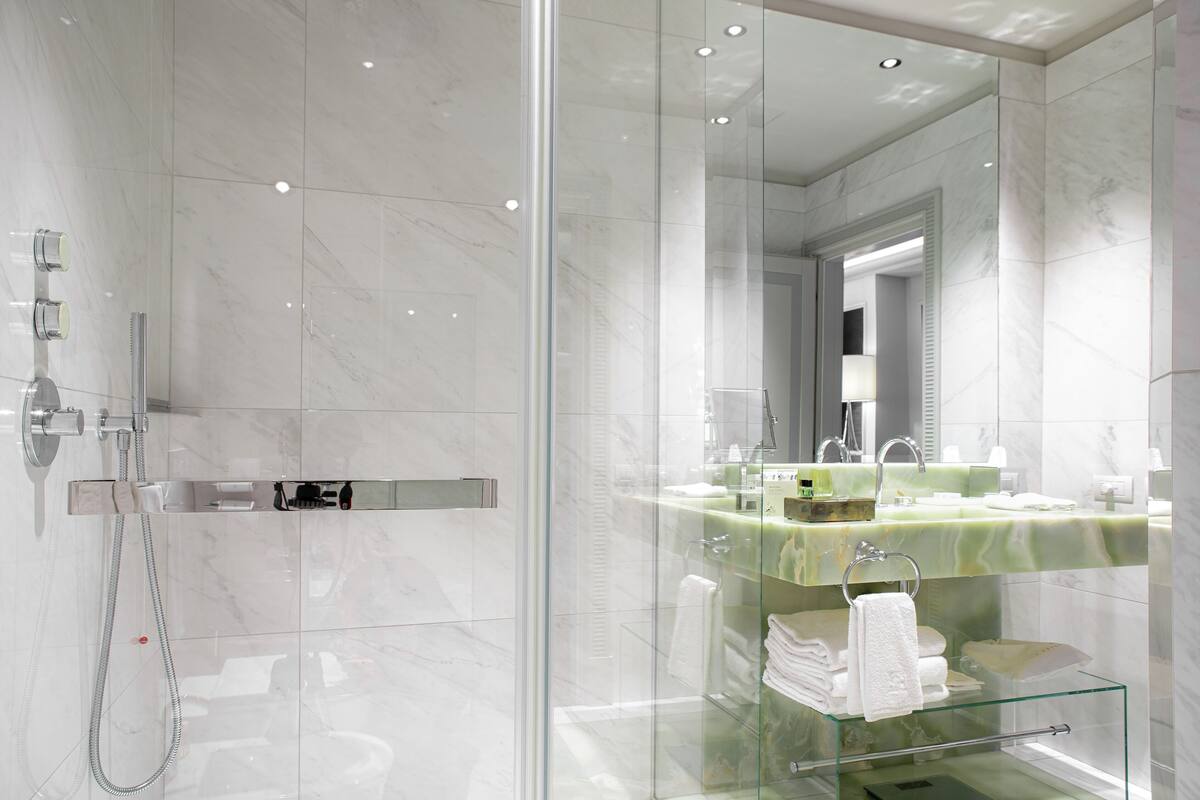 A modern bathroom with a glass-enclosed shower, a glass-topped vanity with a green marble countertop, and a large mirror.