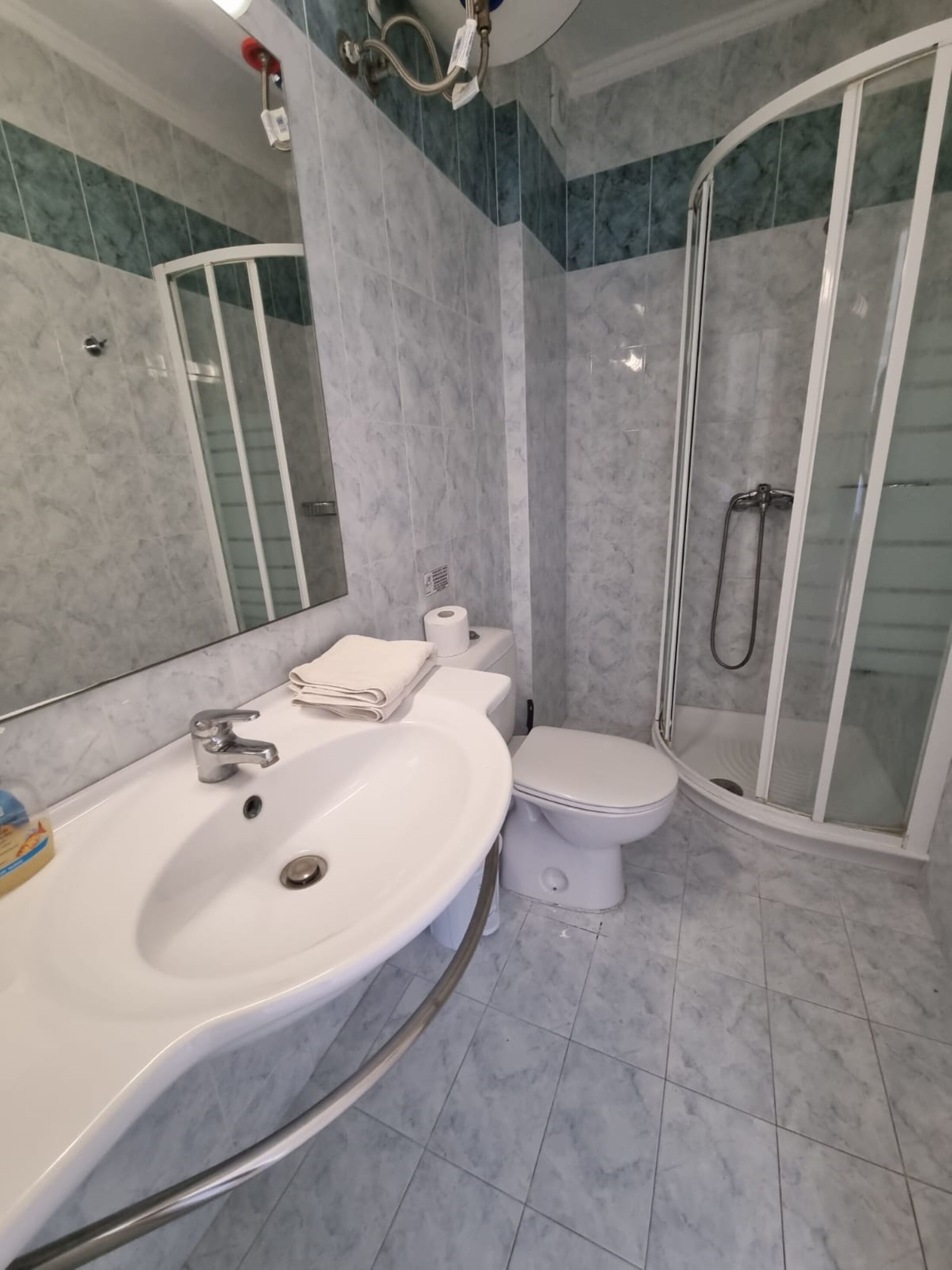 Un baño con lavamanos blanco, inodoro y ducha con mampara de vidrio.