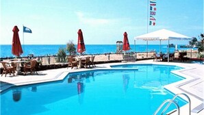 Ein Swimmingpool mit Liegestühlen und Sonnenschirmen, eine Flagge und der Blick aufs Meer.