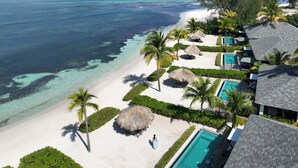An aerial view of a resort with a beach, clear blue waters, and a swimming pool.