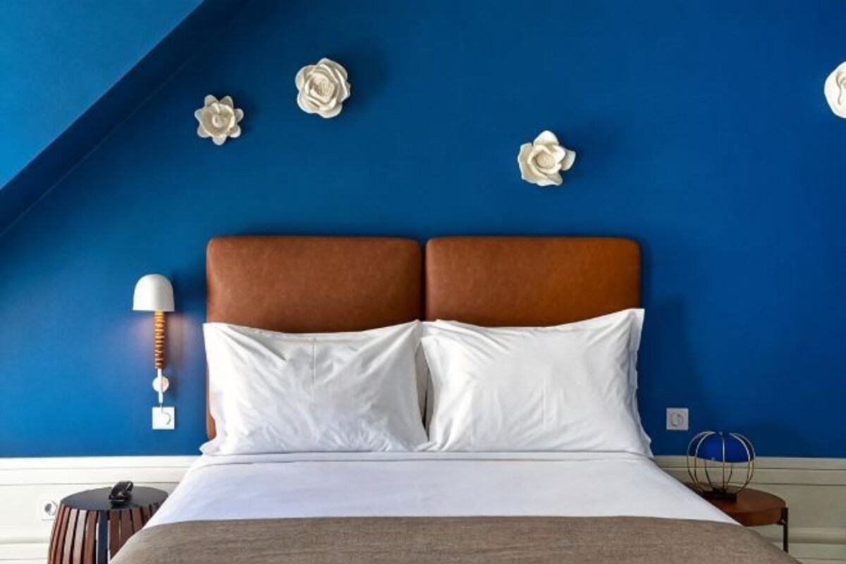 Un dormitorio con cama, mesita de noche, lámpara y flores decorativas en la pared.