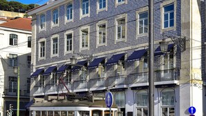 A yellow tram on a street with a building featuring blue and white tiles and a balcony. - My Story Hotel Figueira (Lisbon)