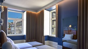 A hotel room with two beds, a large window with a view of buildings, and a mirror reflecting the room. - My Story Hotel Figueira (Lisbon)