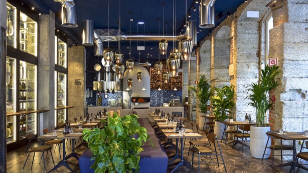 A spacious restaurant with long tables, hanging lights, and a central seating area. - My Story Hotel Figueira (Lisbon)