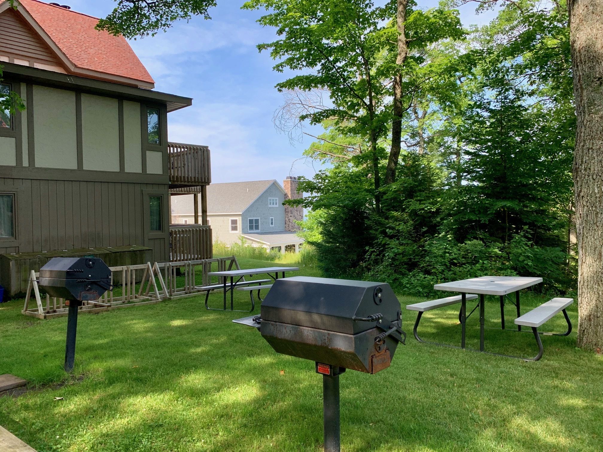 Un patio trasero con una parrilla, mesas de picnic y una terraza de madera.