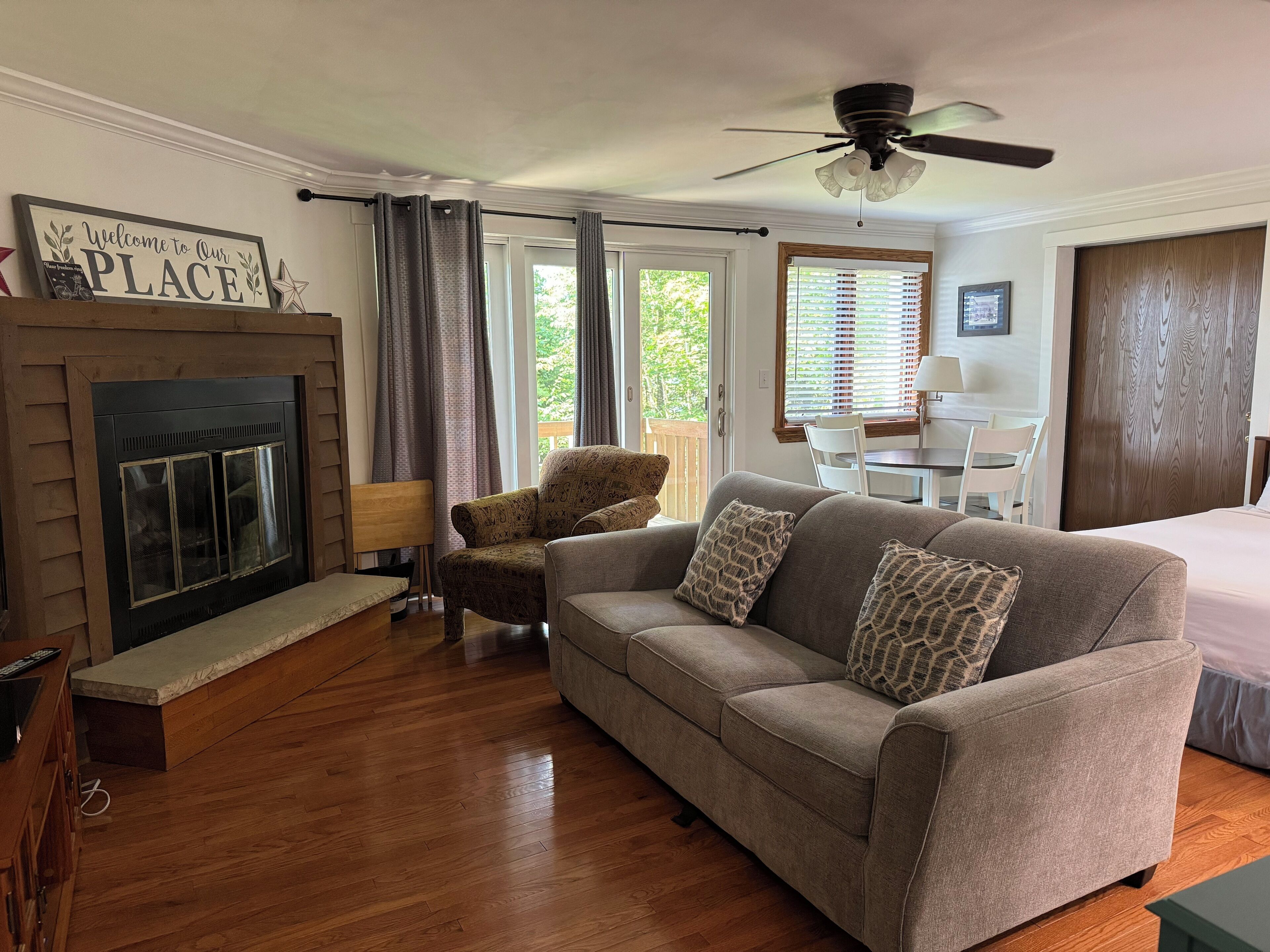 A cozy living room with a fireplace, a sofa, a patterned armchair, and a ceiling fan.