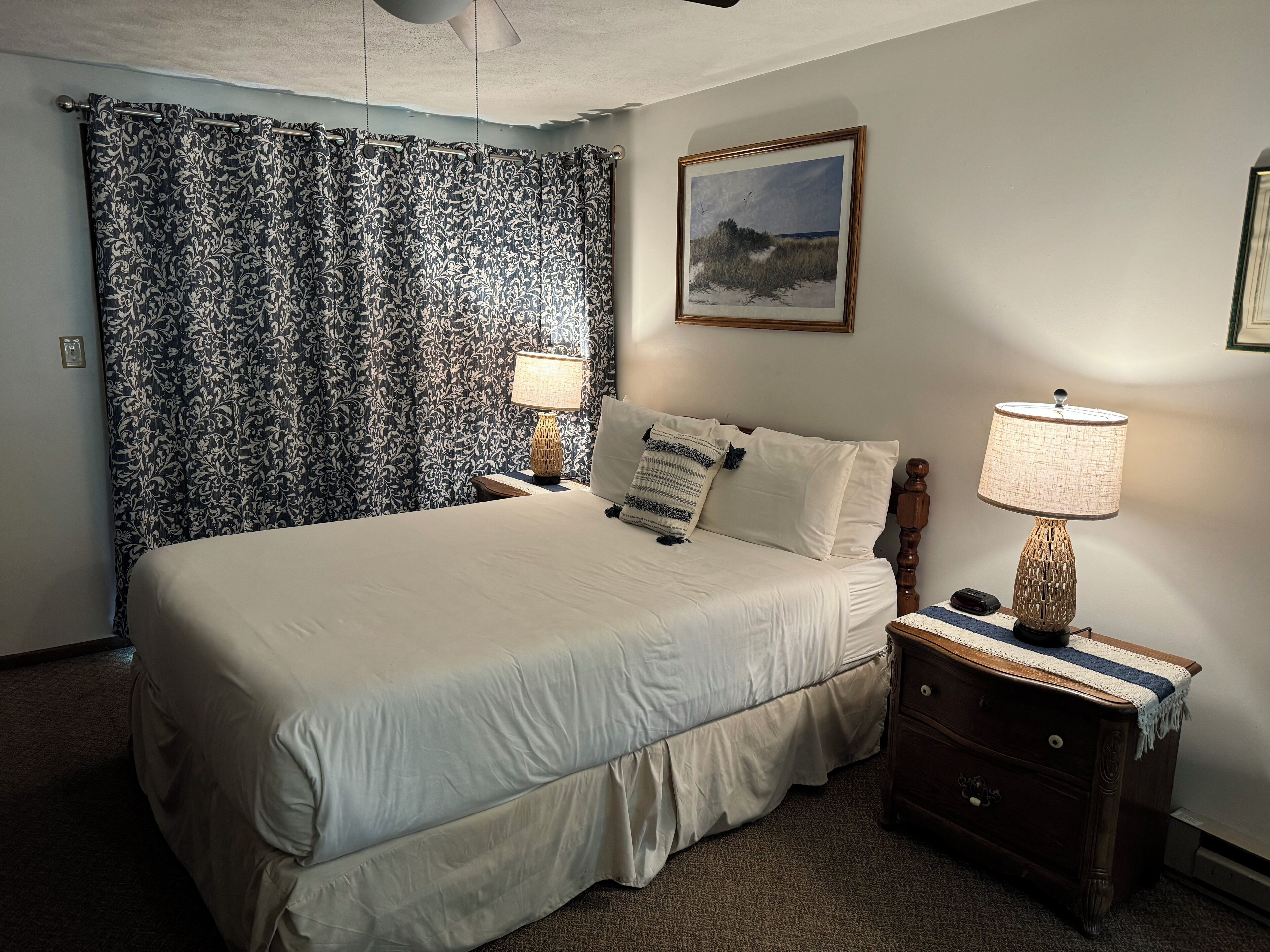 A neatly made bed with white linens, a nightstand with a lamp, and a framed picture on the wall.