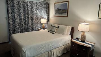 A neatly made bed with white linens, a nightstand with a lamp, and a framed picture on the wall.
