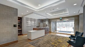 A modern hotel lobby with a reception desk, a 'Welcome to the Heartland' sign, a shop, and a seating area. - Hampton Inn by Hilton Peterborough (Peterborough)