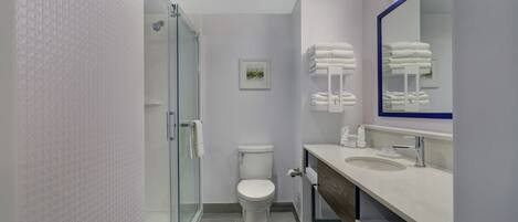 A modern bathroom with a glass shower enclosure, a white toilet, a sink with a mirror, and neatly stacked towels.