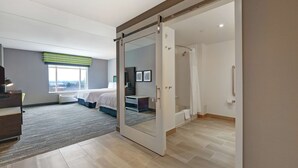 A modern hotel room with a sliding door leading to a shower area, a bed with a view, and a desk with a chair. - Hampton Inn by Hilton Peterborough (Peterborough)