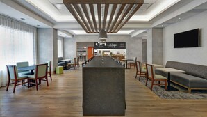 A modern hotel lobby with a central bar, seating areas, and a flat-screen TV on the wall. - Hampton Inn by Hilton Peterborough (Peterborough)