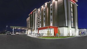 A modern hotel with a prominent red and white facade, multiple floors, and a well-lit entrance area. - Hampton Inn by Hilton Peterborough (Peterborough)