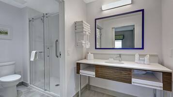 Un baño moderno con cabina de ducha de vidrio, un lavamanos blanco sobre un mueble de madera y un espejo grande con marco púrpura.