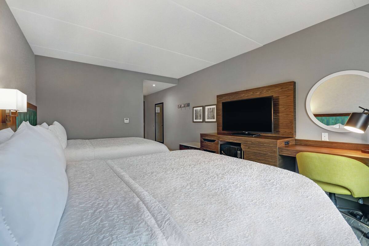 A hotel room with two beds, a TV, a desk, and a chair.