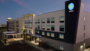 A modern hotel building with a prominent 'TRU by Hilton' sign, a covered outdoor seating area, and a parking lot. - Tru by Hilton San Antonio Lackland Sea World (San Antonio)