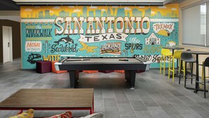 A pool table in a room with a mural depicting Texas landmarks and a city skyline. - Tru by Hilton San Antonio Lackland Sea World (San Antonio)