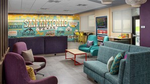 A lounge area with seating, a mural, and a view of the outside. - Tru by Hilton San Antonio Lackland Sea World (San Antonio)