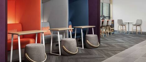 A modern lounge area with seating and tables, featuring a herringbone-patterned floor and a mix of red and blue seating areas.