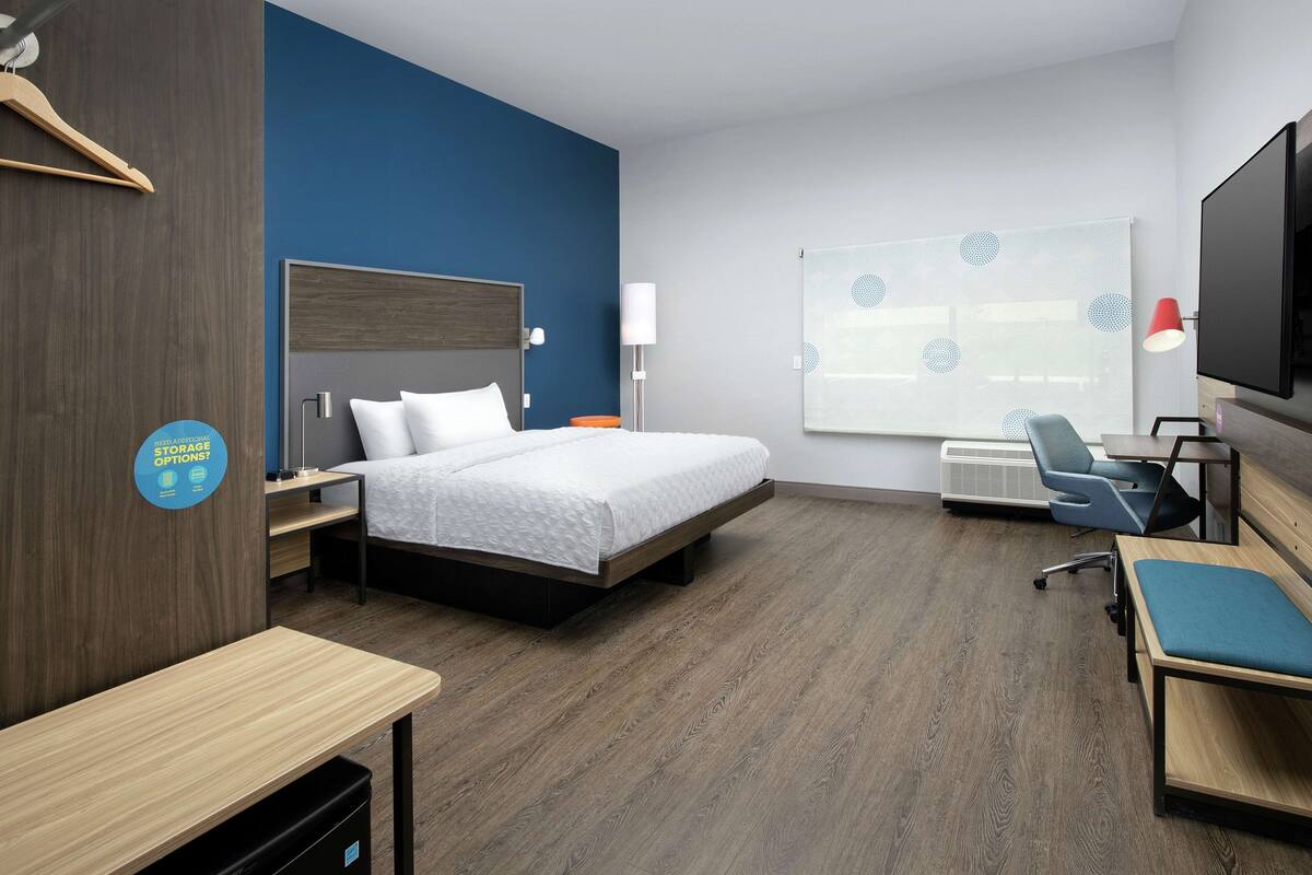 Ein modernes Hotelzimmer mit Bett, Schreibtisch, Stuhl und einem großen Fenster mit Jalousien.