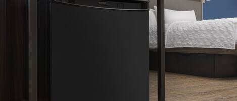 Un refrigerador negro compacto sobre una estantería de madera en una habitación de hotel con una cama y una mesita de noche.