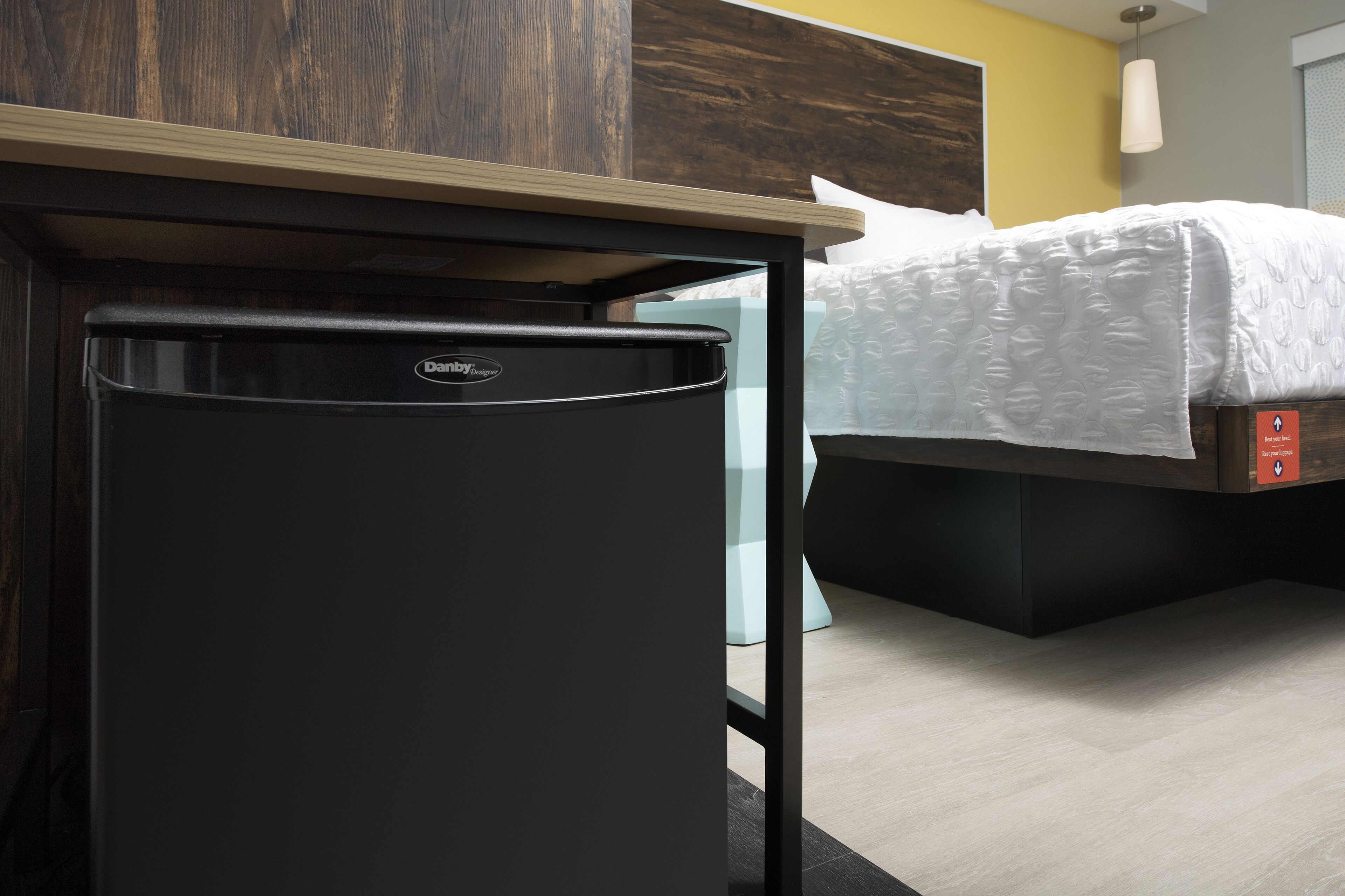 A compact refrigerator in a hotel room with a bed and a wooden headboard.