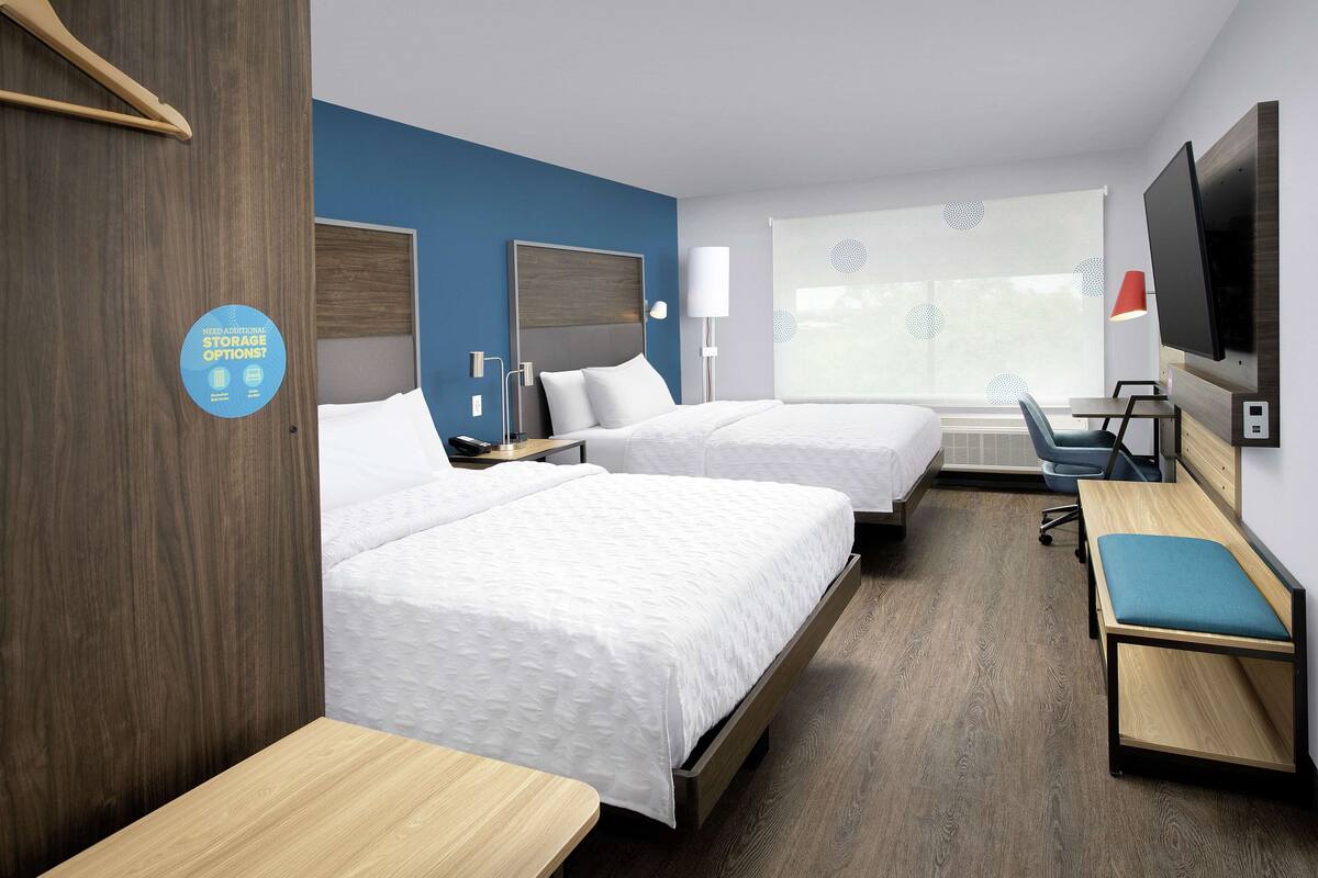 Ein Hotelzimmer mit zwei Betten, einem Schreibtisch, einem Fernseher und einem Fenster mit Jalousien.