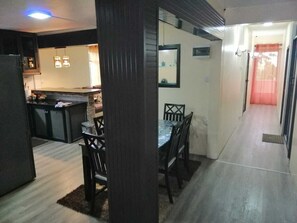 A modern kitchen with dark cabinetry, a dining area with a table and chairs, and a hallway leading to a door.
